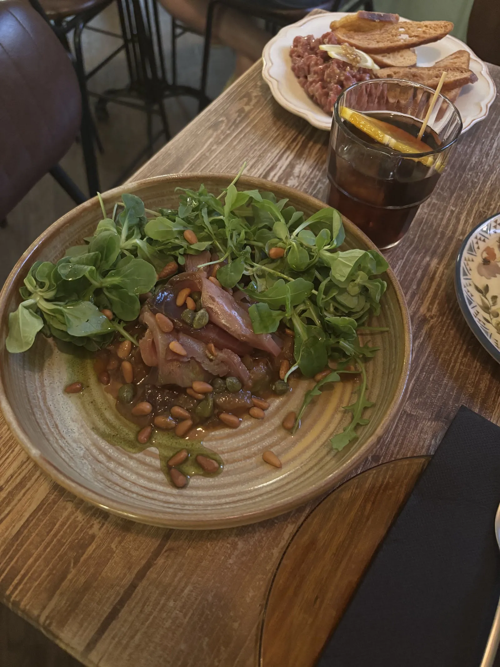 A plate with greens and pine nuts, next to a vermouth