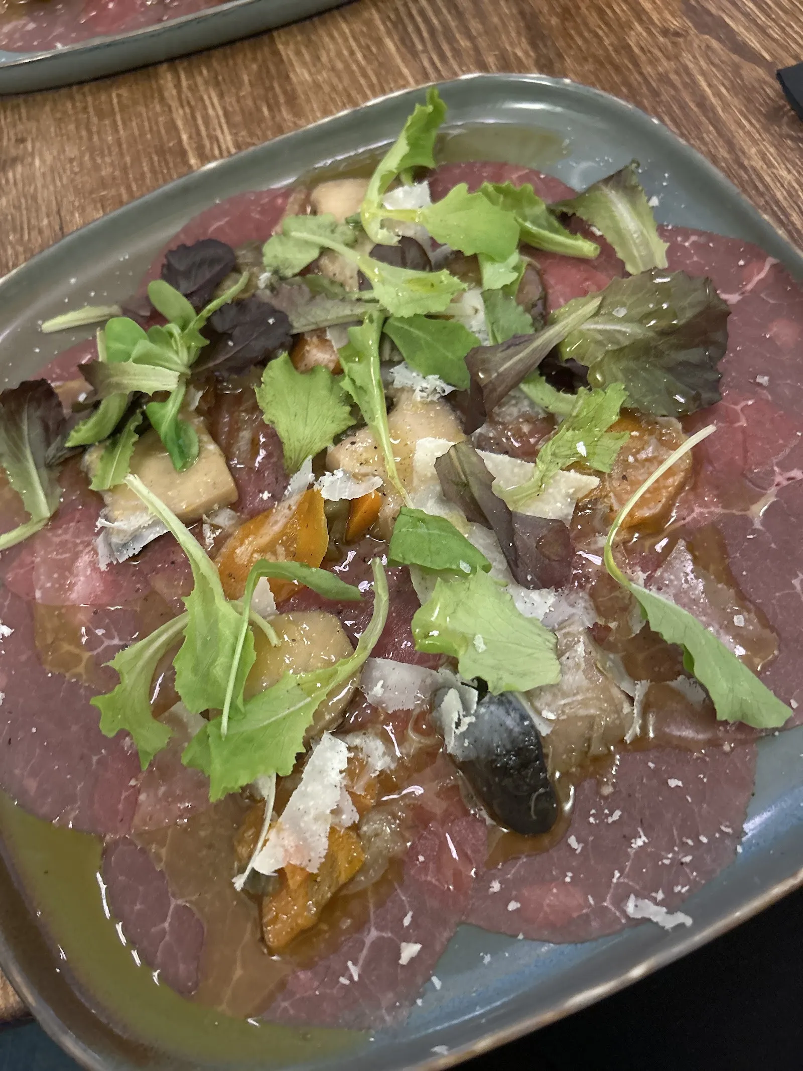 A plate of thinly sliced meat with green shoots